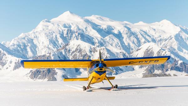 A yellow plane has landed in front of a large, jagged mountain