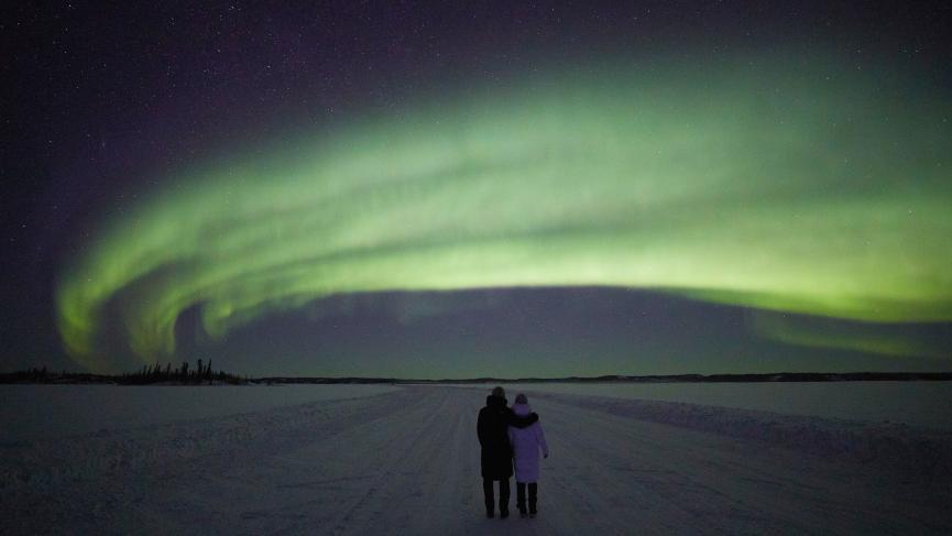Couple stands together under a green arc of northern lights