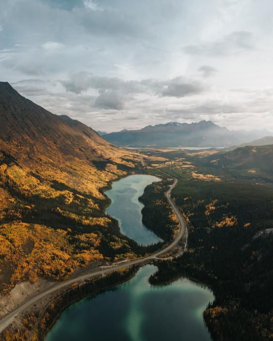 Two teal lakes on either side of a highway next to a mountainside